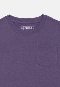 Μωβ κοντομάνικη μπλούζα από βαμβάκι, με στρογγυλή λαιμόκοψη, μικρό τσεπάκι στο στήθος και ετικέτα με πληροφορίες μεγέθους.