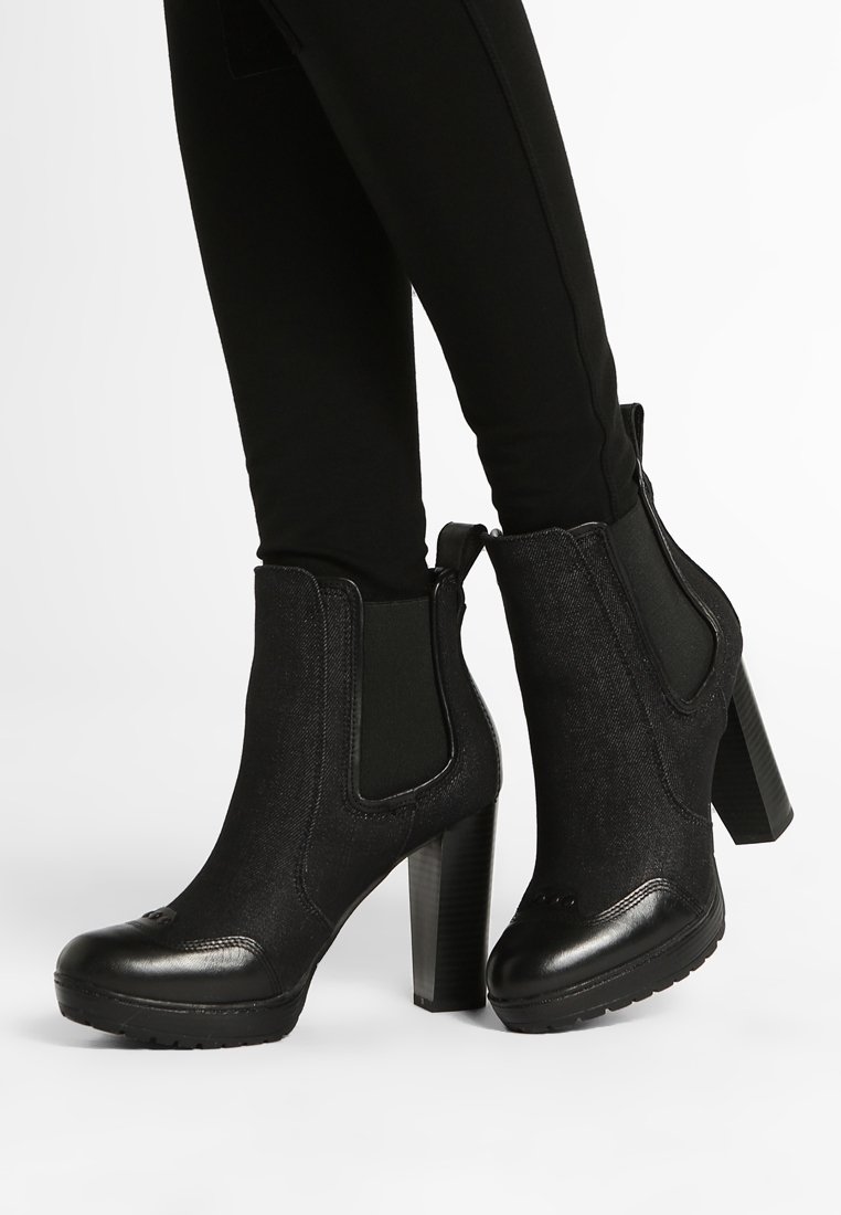Botas negras hasta el tobillo con un upper de tejido texturizado, paneles laterales elásticos y un tacón grueso. Cuenta con una puntera redondeada y suela de goma.