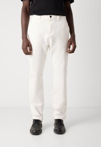 Hvite bomullsbukser med en rett ben-design, med frontknapp og sidelommer, kombinert med svarte skinnsko.