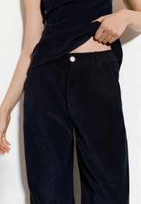 Morske modre kord hlače z ravnim krojem, teksturiranim žametam in sprednjim zaponko s srebrnim detajlom.