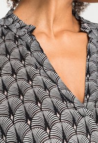 Tissu en noir et blanc à motif de vagues, avec un col en V profond et un col volanté. Texture douce et apparence légère.