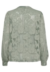 Blusa trasparente di un leggero verde con ricami floreali, maniche lunghe, polsini elasticizzati e dettagli con bottoni. Il design sul retro presenta intricate fantasie di rose.