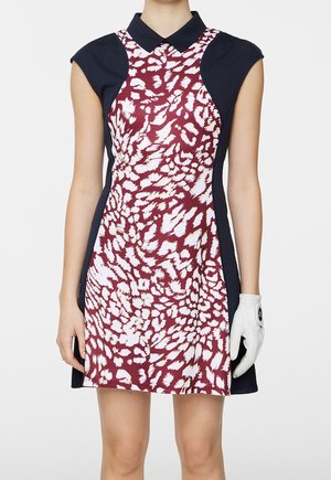 Vestito senza maniche con pannelli laterali e colletto blu navy, centro bordeaux con stampa astratta di animali bianca, indossato da una persona con guanto bianco sulla mano destra.