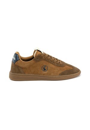 Zapatilla de gamuza marrón con cordones, detalles en marrón oscuro en la puntera y el talón, y un logo circular negro en el lateral sobre fondo blanco.