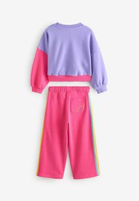 Krāsaini bloku treniņtērps, kas sastāv no purpura džemperis ar rozā piedurknēm un atbilstošiem rozā treniņbikšu ar varavīksnes sānu svītrām un aizmugures kabatas detalizāciju.