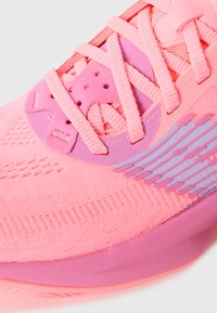 Sportsko i en livlig pink farve med tekstureret mesh-overdel, kontrasterende lilla detaljer og snørelukning med et perforeret design.