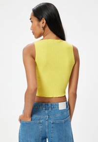 Top corto amarillo con superficie texturizada y dobladillo redondeado, combinado con jeans de mezclilla azul que presentan grandes bolsillos traseros y una sutil marca.