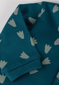 Turquoise knitted cardigan with grey leaf patterns. Features a folded collar and cuffs, showcasing a soft texture and comfortable design.