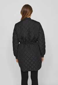 Svart kviltad jacka med åtdragen midja, ribbade ärmslut och midjelängd, med ett diamantmönster och slät yta.