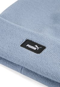 Svijetloplavi pleteni zimski šešir s teksturiranim finišom. Ima crnu pravokutnu oznaku s bijelim "PUMA" brandom i logotipom.