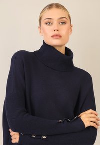 Marineblaues Rollkragensweatshirt, übergroße Passform, gerippte Textur an den Ärmeln, mit silbernen Knopfdetails an den Manschetten für zusätzlichen Akzent.