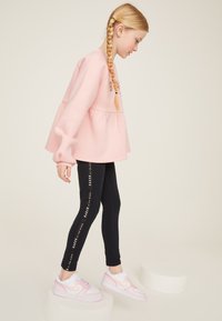 Rozā džemperis ar volāniem apakšmalā, kombinēts ar melnām legingām ar baltu tekstu. Apavi: rozā un baltas Nike sporta kurpes.