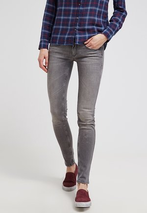 Person wearing gray skinny jeans, a blue and red plaid shirt, and burgundy slip-on shoes walking forward.