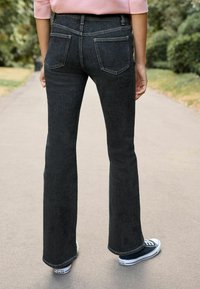 Czarne jeansy dzwonowe z wysokim stanem, z dwiema kieszeniami z tyłu i subtelną teksturą. Zestawione z czarno-białymi trampkami.