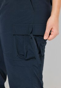 Marina blå cargo-byxor gjorda av ett lätt material som har en stor ficka med lock, en knutdetalj och strömlinjeformad sömnad.