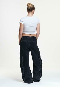 White cropped t-shirt and black baggy cargo pants with multiple pockets. Fabric appears soft, with a relaxed fit and minimal detailing.