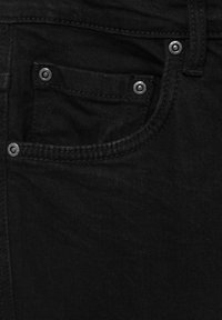 Tissu en denim noir avec une petite poche avant ornée de rivets métalliques et des coutures détaillées près de la ceinture et de la boucle de ceinture.