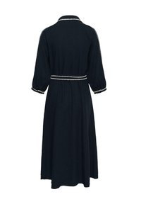 Vestido largo azul marino con mangas hasta el codo, ribete blanco en forma de zigzag en el cuello, los puños y el cinturón de la cintura, visto desde atrás.