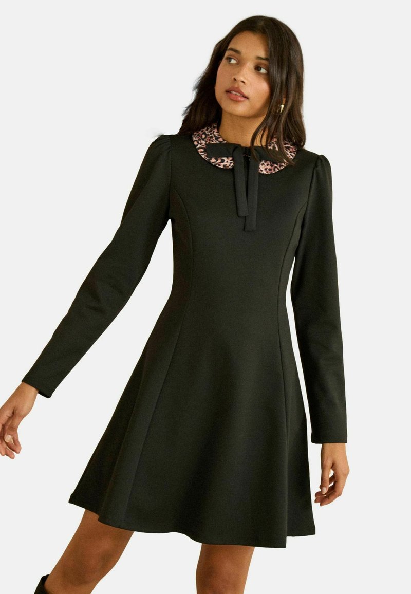 Rochie neagră cu mâneci lungi, cu fustă evazată, cu guler cu imprimeu leopard și detaliu de fundă la nivelul gâtului. Textură fină a materialului.