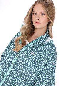 Jachetă ușoară cu bază de culoare verde-albăstrui închis, având un imprimeu îndrăzneț leopard aqua, glugă reglabilă și închidere frontală cu fermoar.