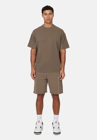 Set van een bruine katoenen t-shirt en shorts, met contrasterende stiksels, een relaxte pasvorm en een geribbelde kraag. Gedirigeerd met witte sneakers en sokken.