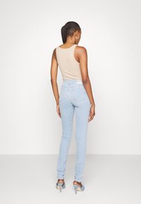 Top sin mangas beige combinado con jeans ceñidos de color azul claro. Los jeans tienen una cintura alta y bolsillos traseros, con una textura de tela suave.