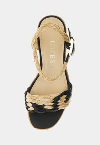 Sandale plateforme noire avec des brides en fibre naturelle tressée, une semelle intérieure beige lisse et une boucle latérale pour un ajustement réglable.