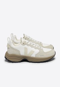 Beige and white sneakers with a mesh upper, suede accents, and a thick brown sole. Features laces and pull tabs for easy wear.