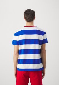 Blå och vit randig t-shirt med röd krage, tillverkad av bomull. Designen har horisontella ränder i växelvis färger.