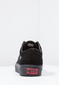 Schwarzer Wildleder-Sneaker mit gepolstertem Schaft, weißen Nähten, Gummisohle und rotem Vans-Logo an der Ferse. Flaches Design.