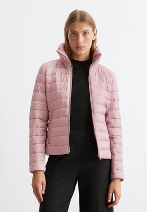 Gepolsterte hellrosa Jacke mit hohem Kragen, ausgestattet mit horizontalen Steppnähten, einem Frontreißverschluss und seitlichen Taschen, getragen über einem schwarzen Oberteil.