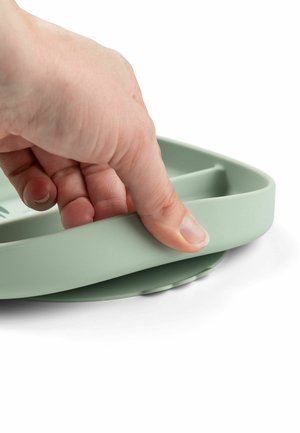 Vihreä silikoninen alusta, jossa on pyöristetty suorakulmainen muoto. Päällä teksturoitu pinta. Käsi tarttuu reunaan tukevasti.