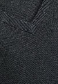 Tissu tricoté gris foncé avec un gros plan sur un détail côtelé de col en V sur un pull ou un vêtement.