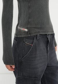 Langsleeve ribbed antracietgrijze top gecombineerd met donkergrijze cargobroeken, met rode merketiketten op de kleding.