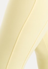 Gros plan sur un tissu jaune avec des lignes de couture visibles suggérant des vêtements moulants, probablement des leggings ou des pantalons.