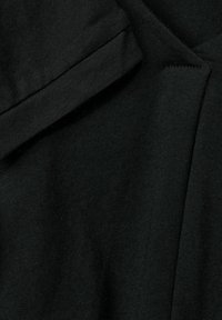 Svart bomullstyg från ett plagg som visar en texturerad yta med en svag glans, vikt med sömmar och råkanter synliga.