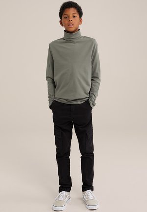 Långärmad, olivgrön polotröja i mjukt material, kombinerad med svarta cargo-byxor med sidofickor och vita sneakers.