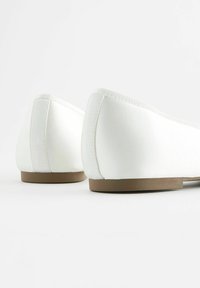 Scarpe bianche flat con una finitura in tessuto liscio, punta rotonda e una suola in gomma marrone bassa. Presentano cuciture sottili e un design elegante.