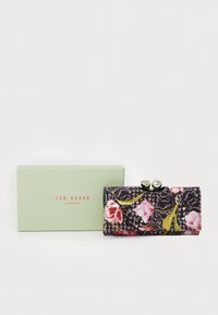 Carteira com padrão floral em tecido preto, com fecho de encaixe com detalhes em prata. Inclui uma caixa verde-clara rotulada "TED BAKER LONDON."