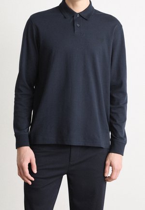 Mann trägt ein einfarbiges dunkelblaues langärmliges Poloshirt mit Kragen und zwei Knöpfen, kombiniert mit passenden dunklen Hosen.