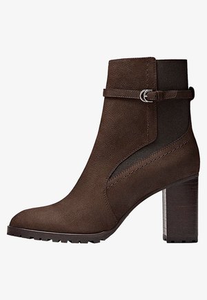 Brauner Wildleder-Stiefelette mit Blockabsatz, seitlichem elastischem Einsatz, dekorativem Riemen und silberner Schnalle, im Profil vor weißem Hintergrund gezeigt.