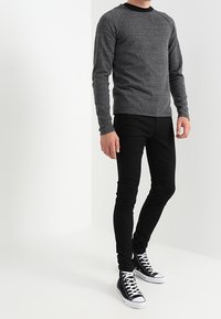 Szara koszula z długim rękawem z czarnym kołnierzykiem, zestawiona z czarnymi rurkowymi dżinsami i czarnymi wysokimi trampkami z białymi podeszwami.