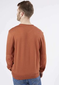 Pull en tricot couleur rouille avec un col rond et des patchs aux coudes ; dispose d'un ourlet et de poignets côtelés ; texture douce et coupe décontractée.