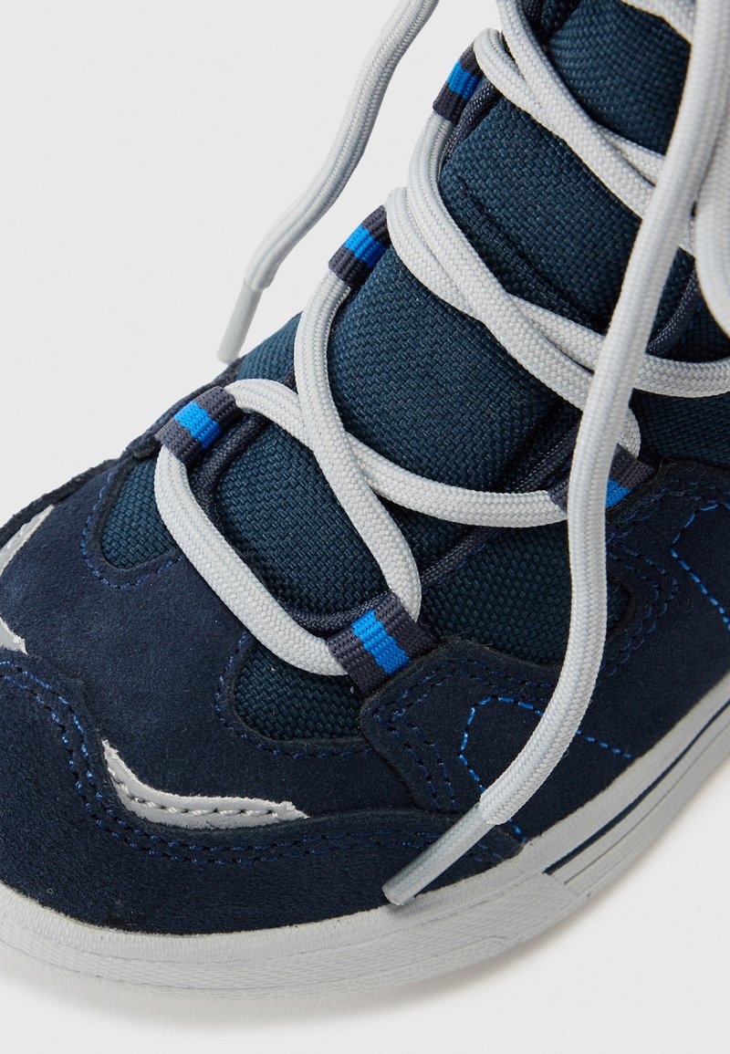Marineblaue Sneaker mit weißen und blau akzentuierten Schnürsenkeln, Obermaterial aus strukturiertem Stoff, Suede-Überzügen und weißer Gummisohle auf weißem Hintergrund.
