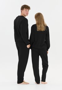 Sort loungewear sæt, der inkluderer en langærmet top og bukser. Stoffet ser blødt ud med en afslappet pasform. Ingen mønstre eller hardware synlige.