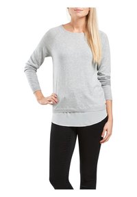 Pull gris clair avec un col rond, des poignets et un ourlet côtelés, superposé sur une chemise gris clair, porté avec un jean skinny noir.
