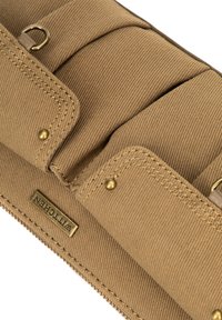 Borsa in cotone beige con tre scomparti, dettagli in ottone e cuciture elaborate. Presenta un'etichetta con logo su una superficie testurizzata.