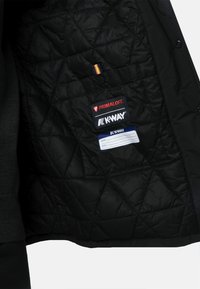Interno della giacca nera trapuntata con etichette Primaloft e K-Way. Presenta una tasca e una linguetta multicolore lungo la cucitura. Texture liscia.