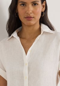 White linen shirt with a button-up front, short sleeves, and a classic collar. The fabric has a slightly textured appearance.