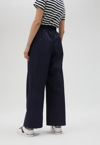 Navy wide-leg pants with an elastic waistband, made of lightweight fabric. Worn with a striped top and white sneakers with blue accents.